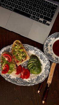 Top view of avocado toast and tea beside a laptop, perfect for a healthy and productive brunch setup.