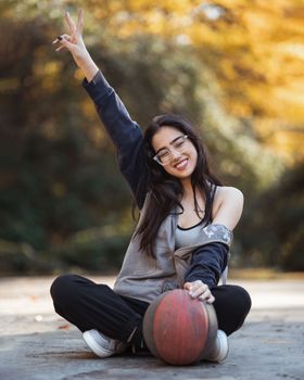 Smiling young woman seated outdoors with a basketball, enjoying a fall day.