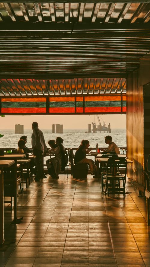 Free Silhouetted group dining at a rooftop restaurant during a warm sunset overlooking the sea. Stock Photo
