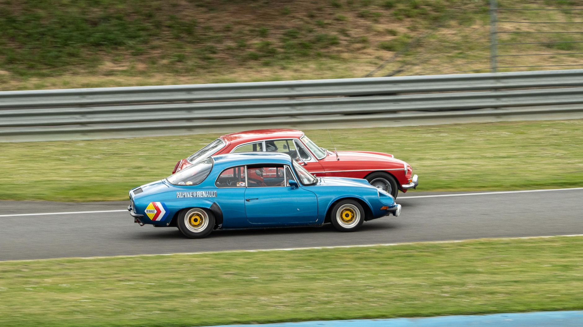 Two classic cars competing in a thrilling race on an outdoor track, showcasing vintage automotive design and speed.