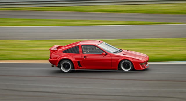A red sports car speeds on a racetrack, capturing the thrill of high-speed racing.