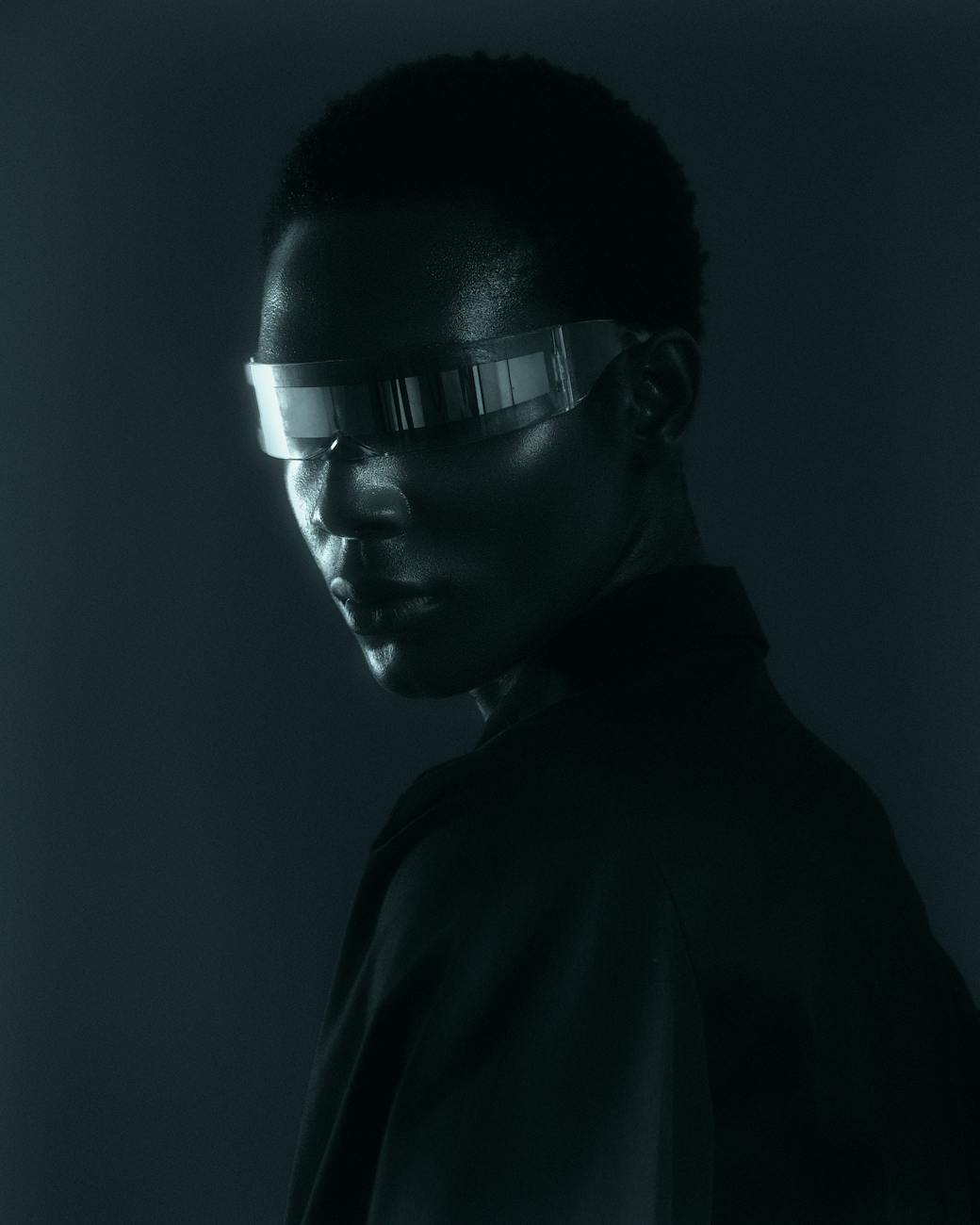 A dramatic and futuristic portrait featuring a model wearing metallic visor glasses in low light.