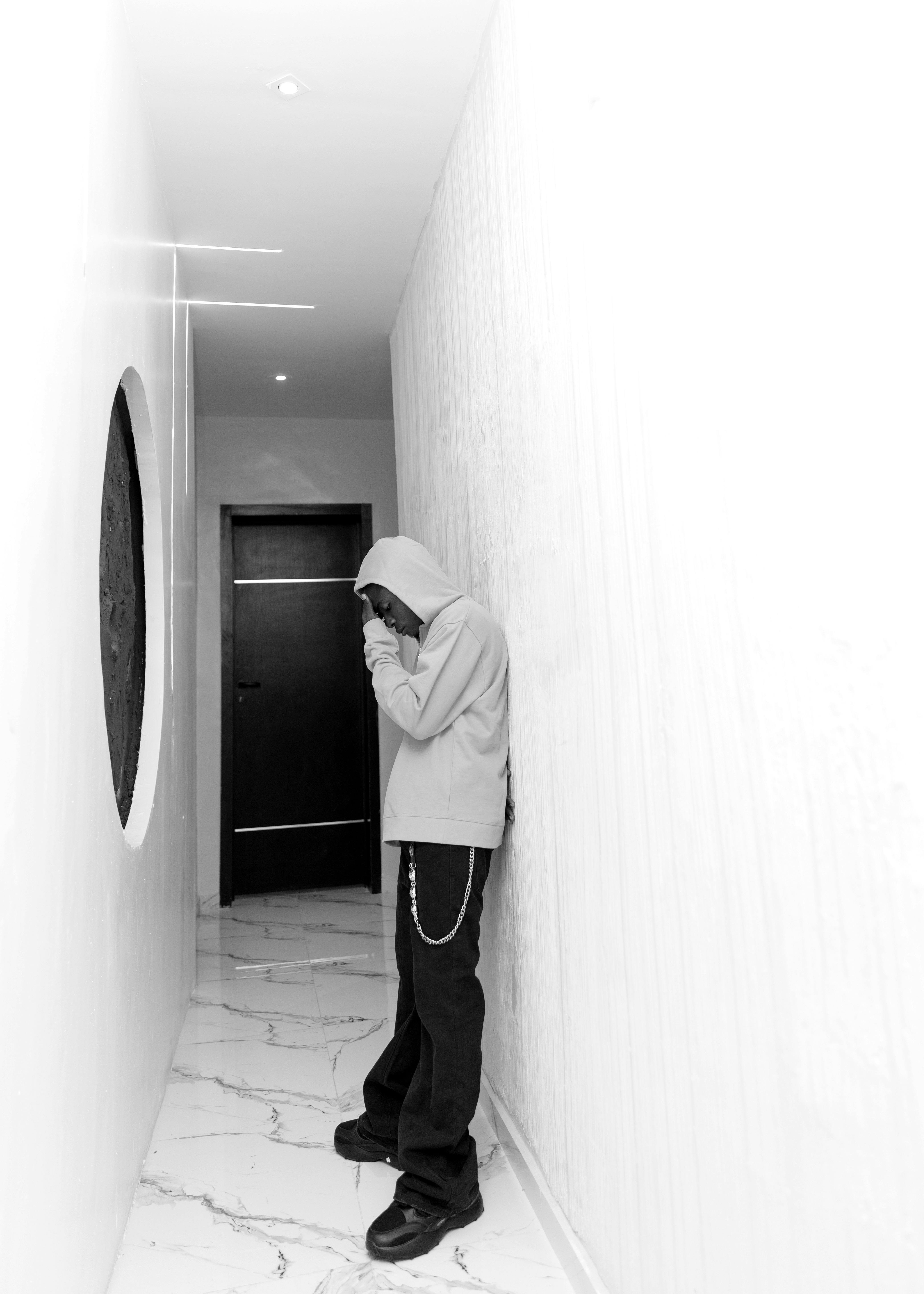 Gratis Persona con una sudadera con capucha parada en un pasillo minimalista, sumida en sus pensamientos. Foto de stock