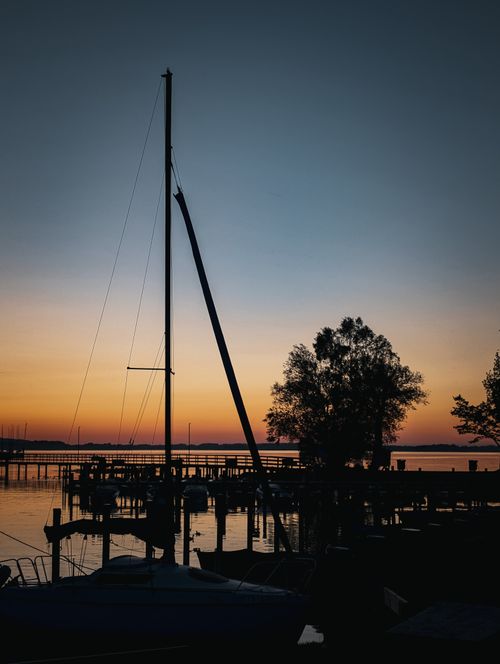 Free Serene sunset view over a Bavarian lake with sailboats and silhouettes creating a calming atmosphere. Stock Photo