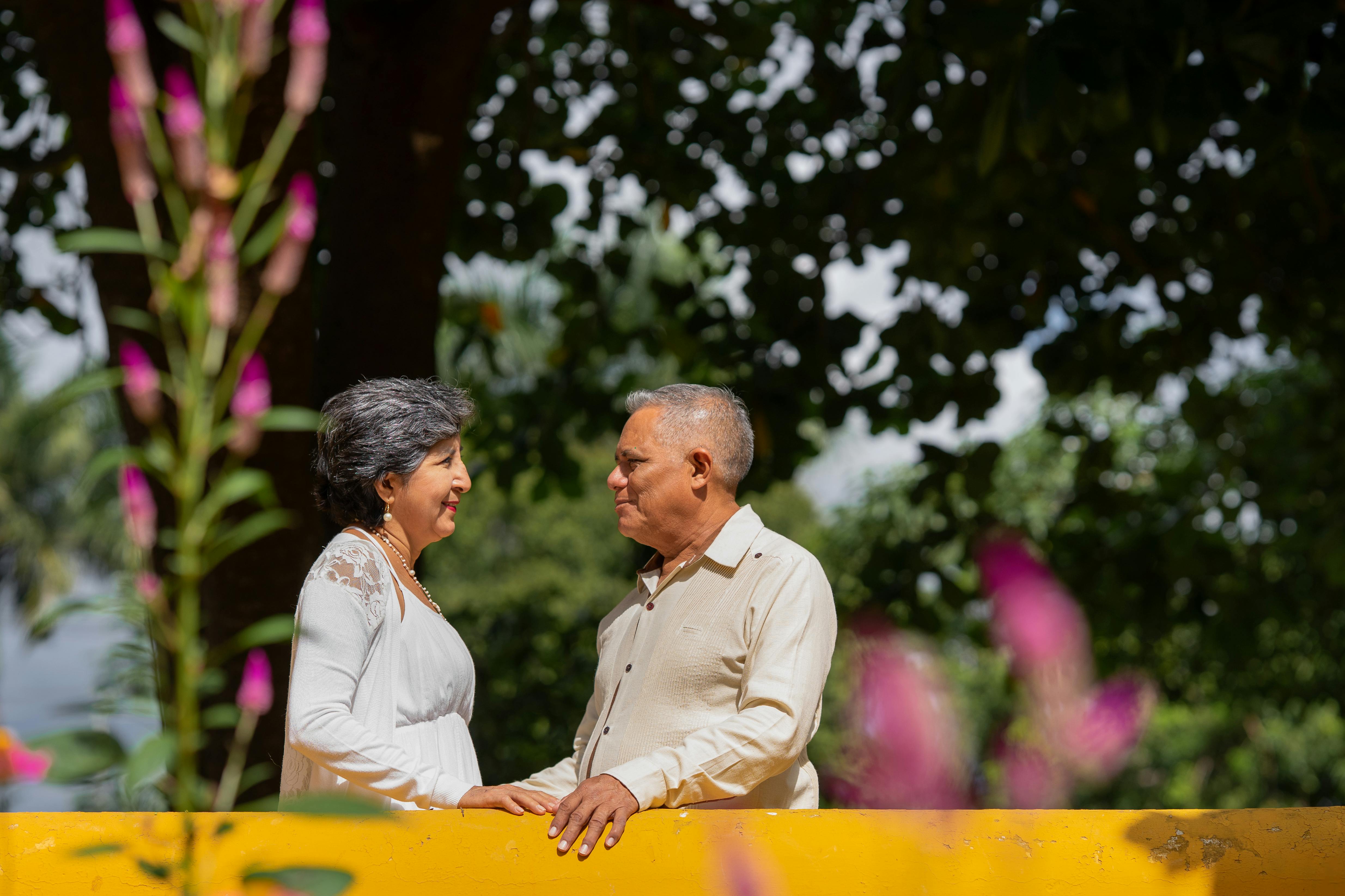 Casal sênior desfrutando de um dia ensolarado em Merida, cercado por flores vibrantes.