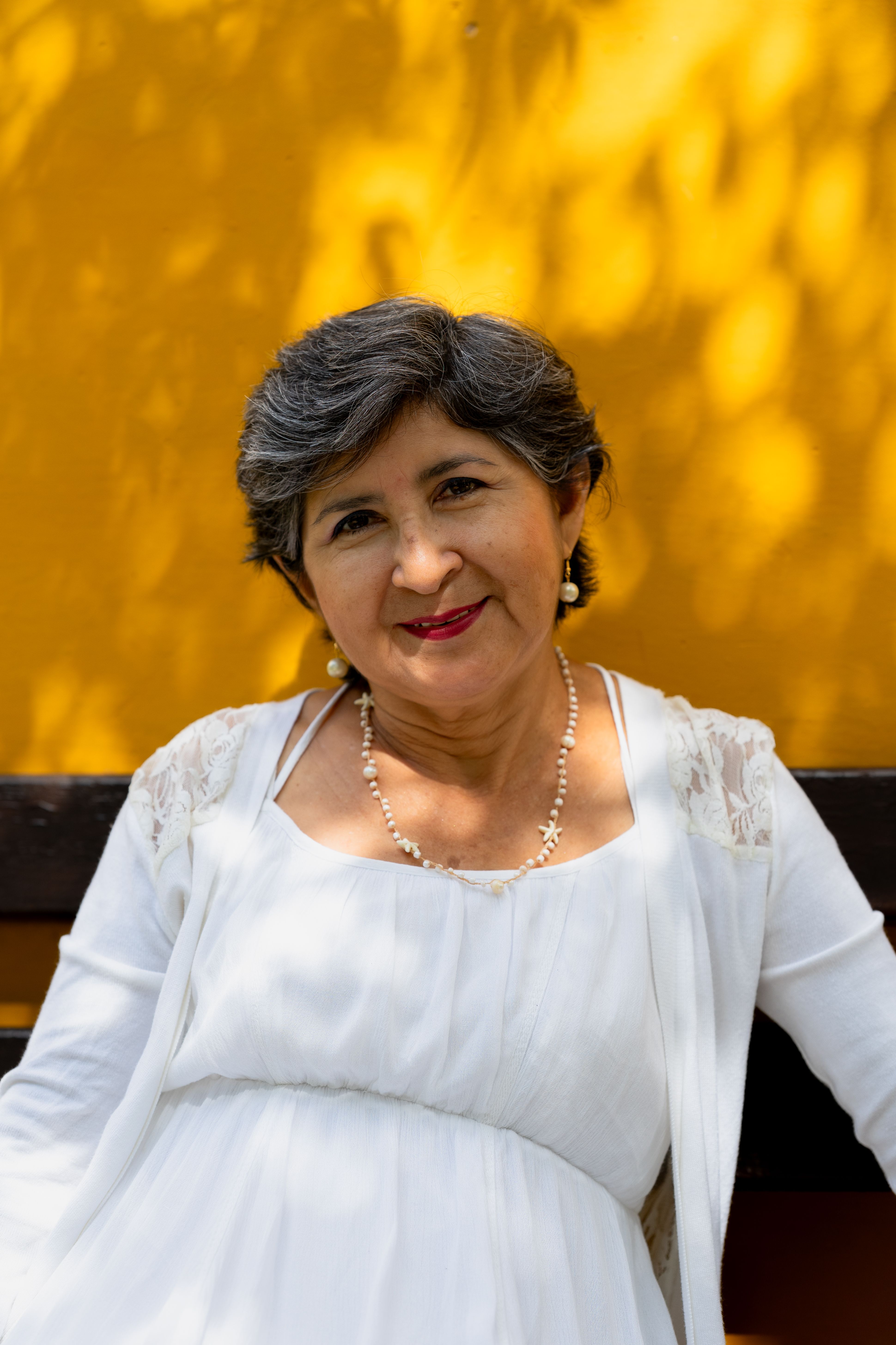 Charming senior woman in white against vibrant yellow backdrop, captured in Merida, Yucatan.