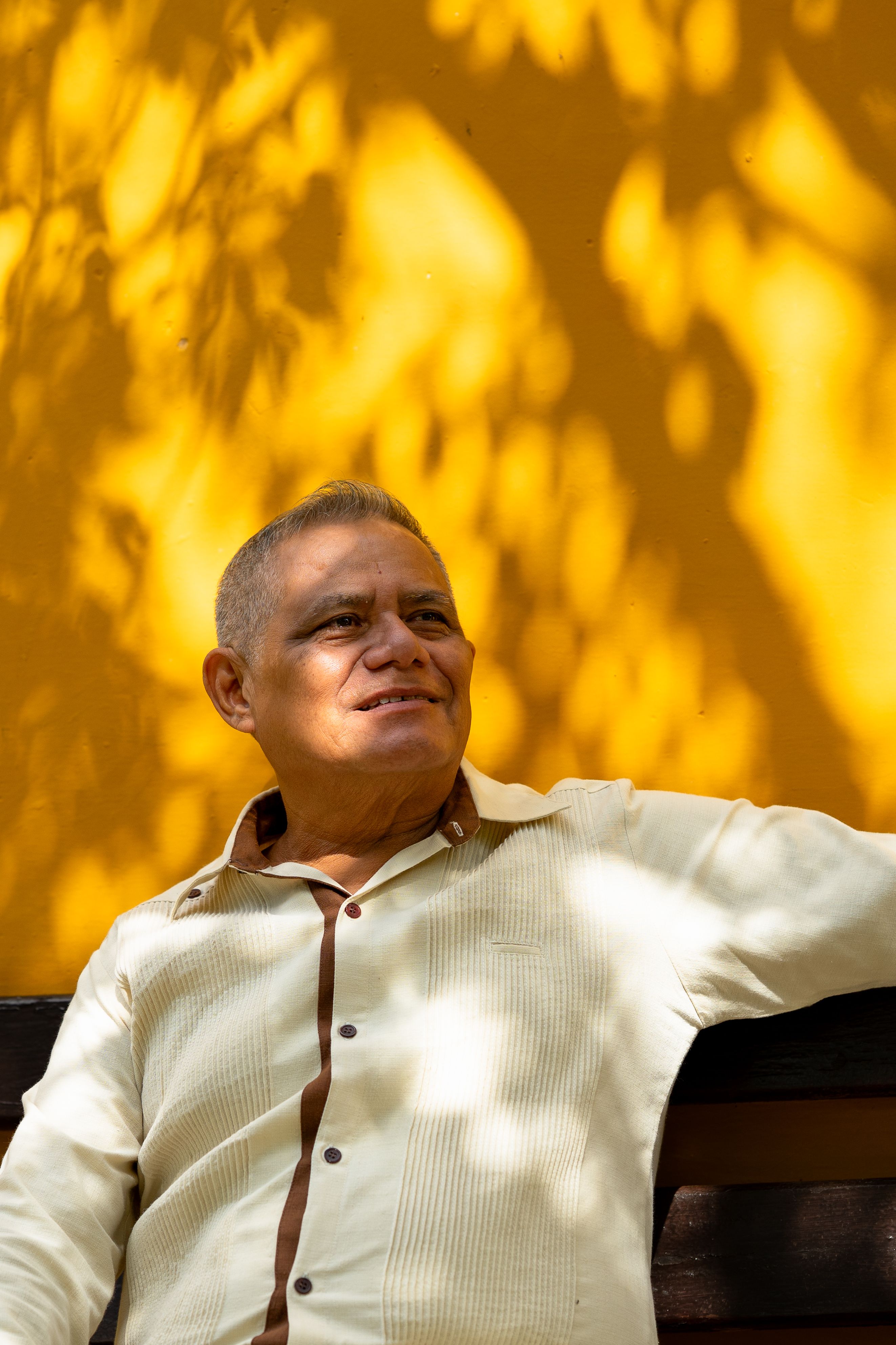 A cheerful man seated against a vibrant yellow wall in Merida, Mexico, enjoying the sunny day.