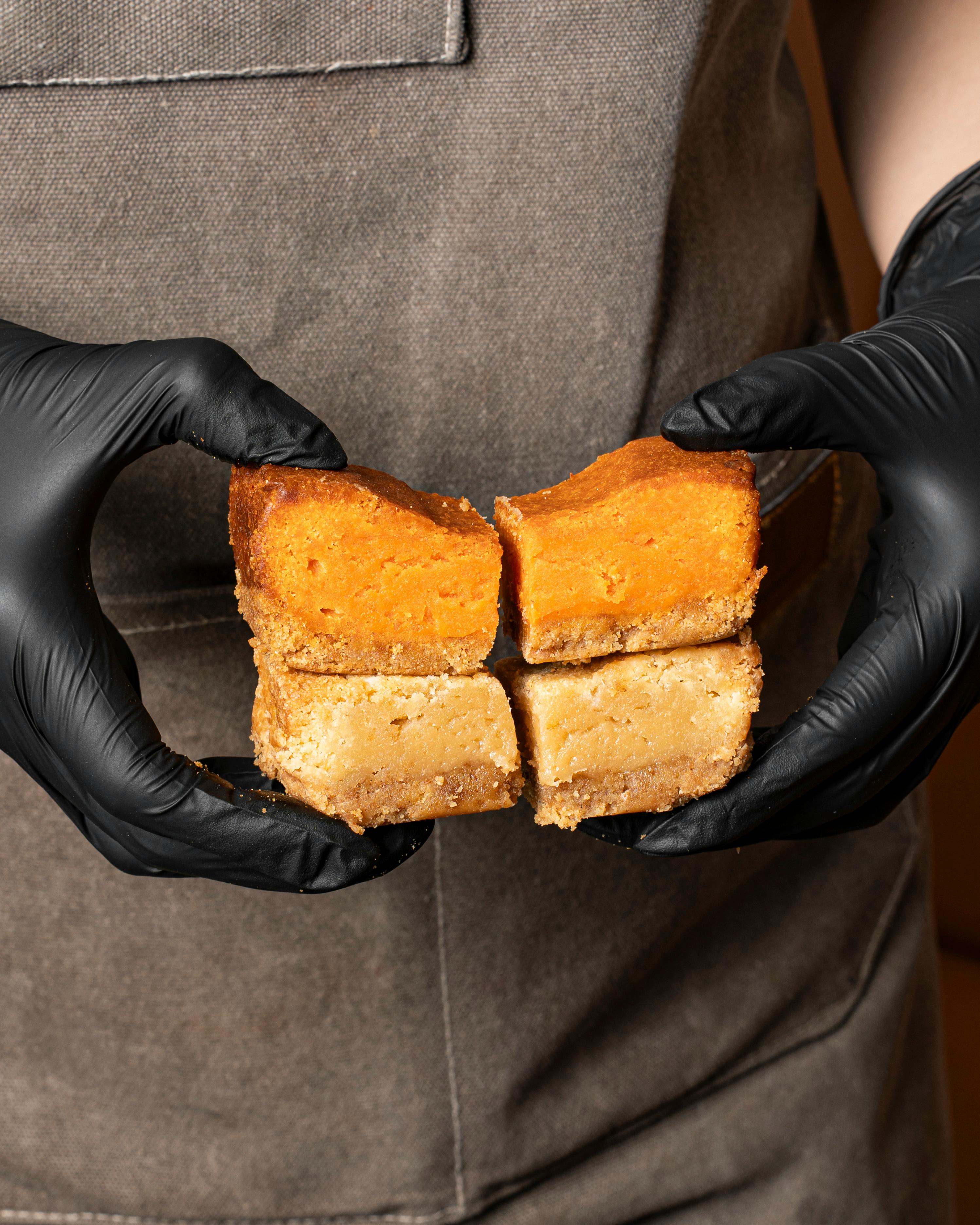 Close-up of cheesecake bars held by a gloved baker, emphasizing texture and craftsmanship.