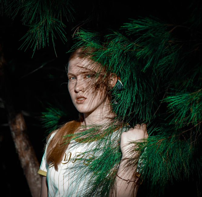 Portrait of a young woman posing with lush greenery in natural lighting.