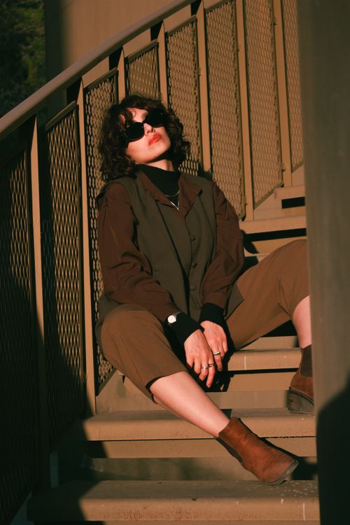 Free Stylish woman in sunglasses poses on an outdoor staircase clad in autumn attire. Stock Photo