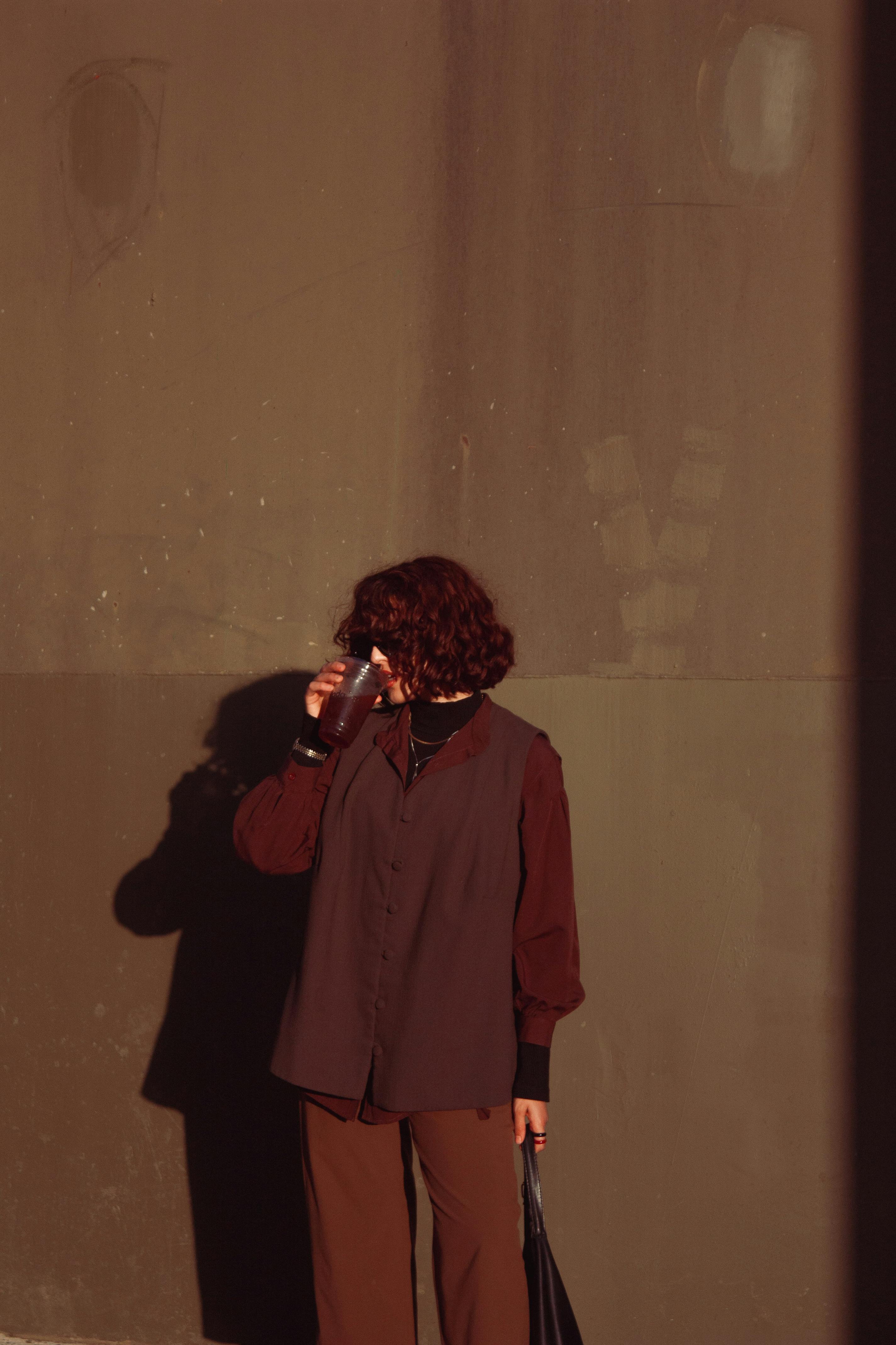 Безкоштовне Жінка у повсякденному вбранні п'є каву біля сонячної стіни. Розслаблена міська атмосфера. стокове фото