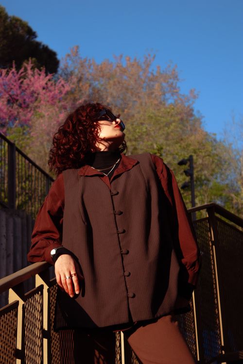 Free Woman with curly hair poses on stairs in autumn attire with colorful foliage background. Stock Photo