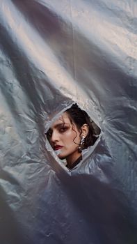 Graceful portrait of a model peeking through a hole in metallic fabric, adding intrigue and style.