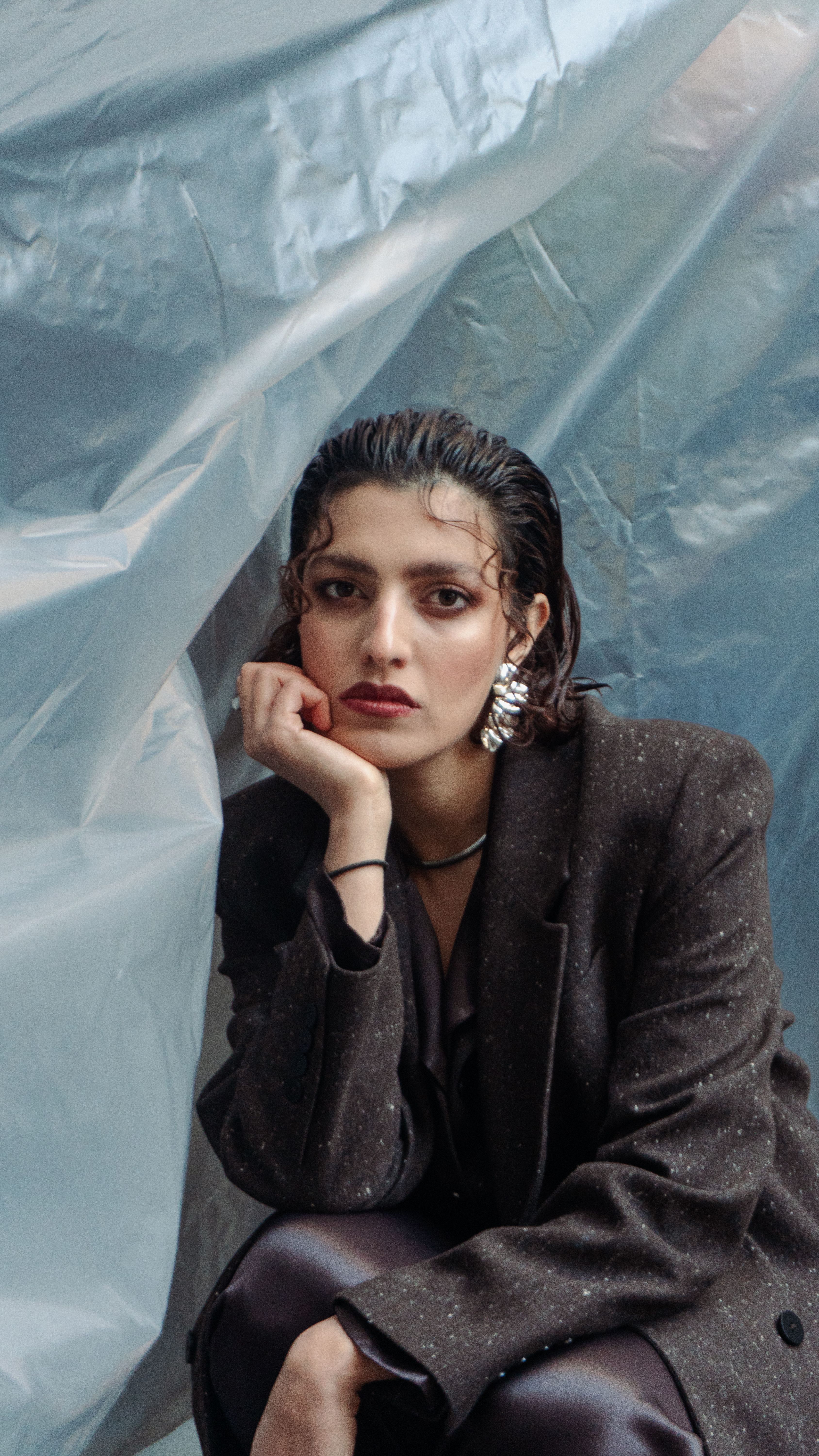 Stylish woman in chic attire posing thoughtfully outdoors against a textured backdrop.