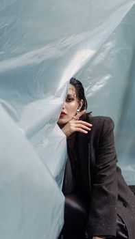 A stylish portrait of a woman half-hidden by plastic sheeting, creating an ethereal effect.