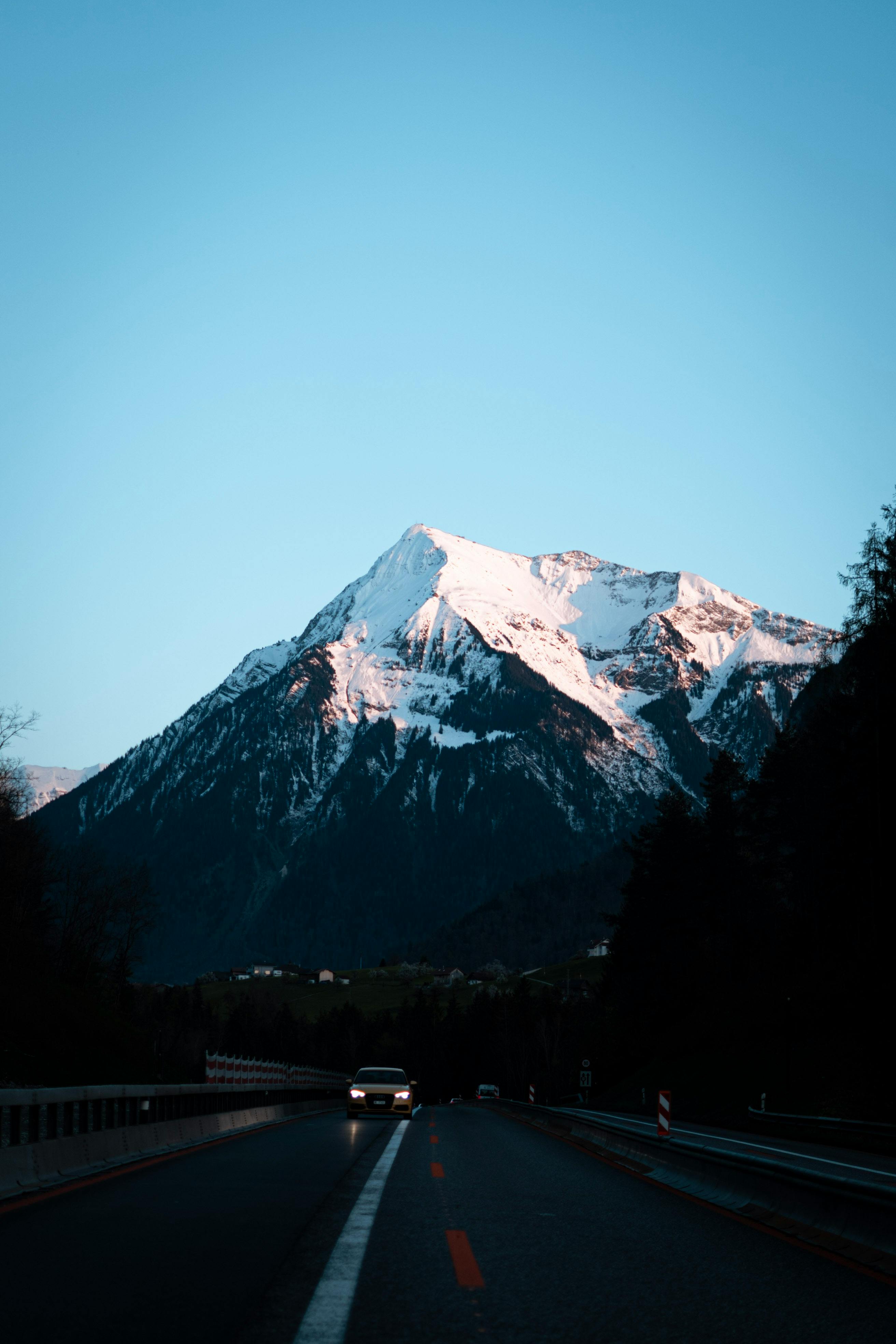Dramatic snowy mountain view during twilight in Switzerland with an oncoming car on a road.