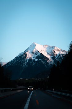 Dramatic snowy mountain view during twilight in Switzerland with an oncoming car on a road.
