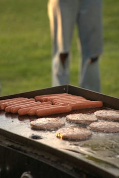 Hot dogs and burgers grilling outdoors on a barbecue on a sunny day.