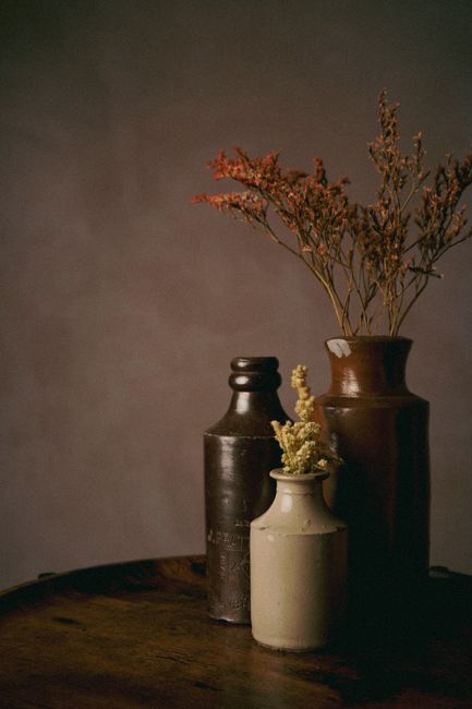 Artistic display of vintage ceramic vases with dried flowers on a rustic table, warm tones.