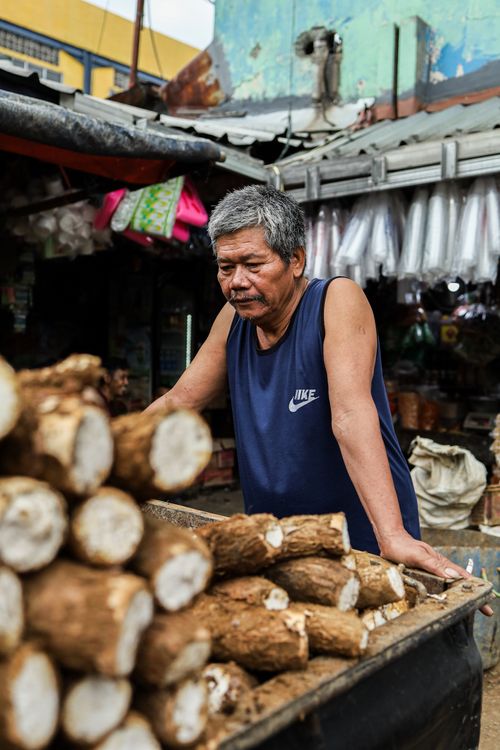 Free Man standing by a cart with yams in an outdoor market setting. Stock Photo