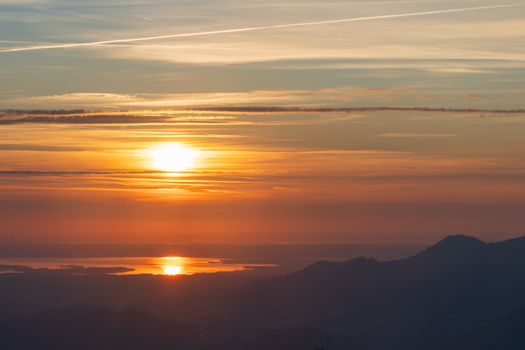 A tranquil sunrise view with vibrant colors reflecting over a mountain range and water.