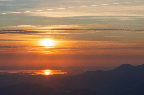 Free A tranquil sunrise view with vibrant colors reflecting over a mountain range and water. Stock Photo