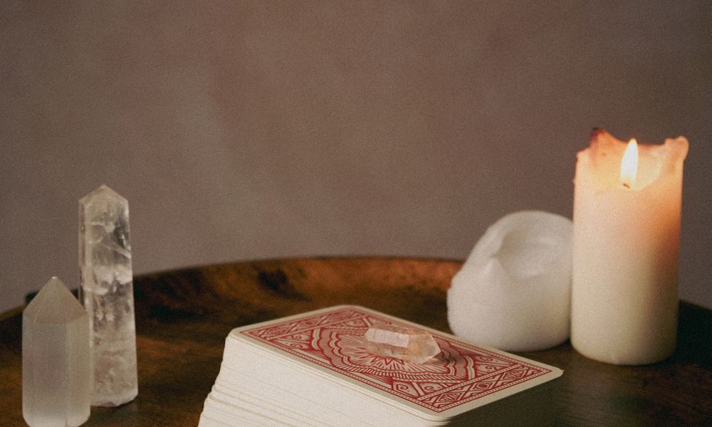 A red-backed tarot deck resting on a wooden table beside a lit candle and crystals, the kind of deck whose 22 trump cards the Destiny Matrix borrows