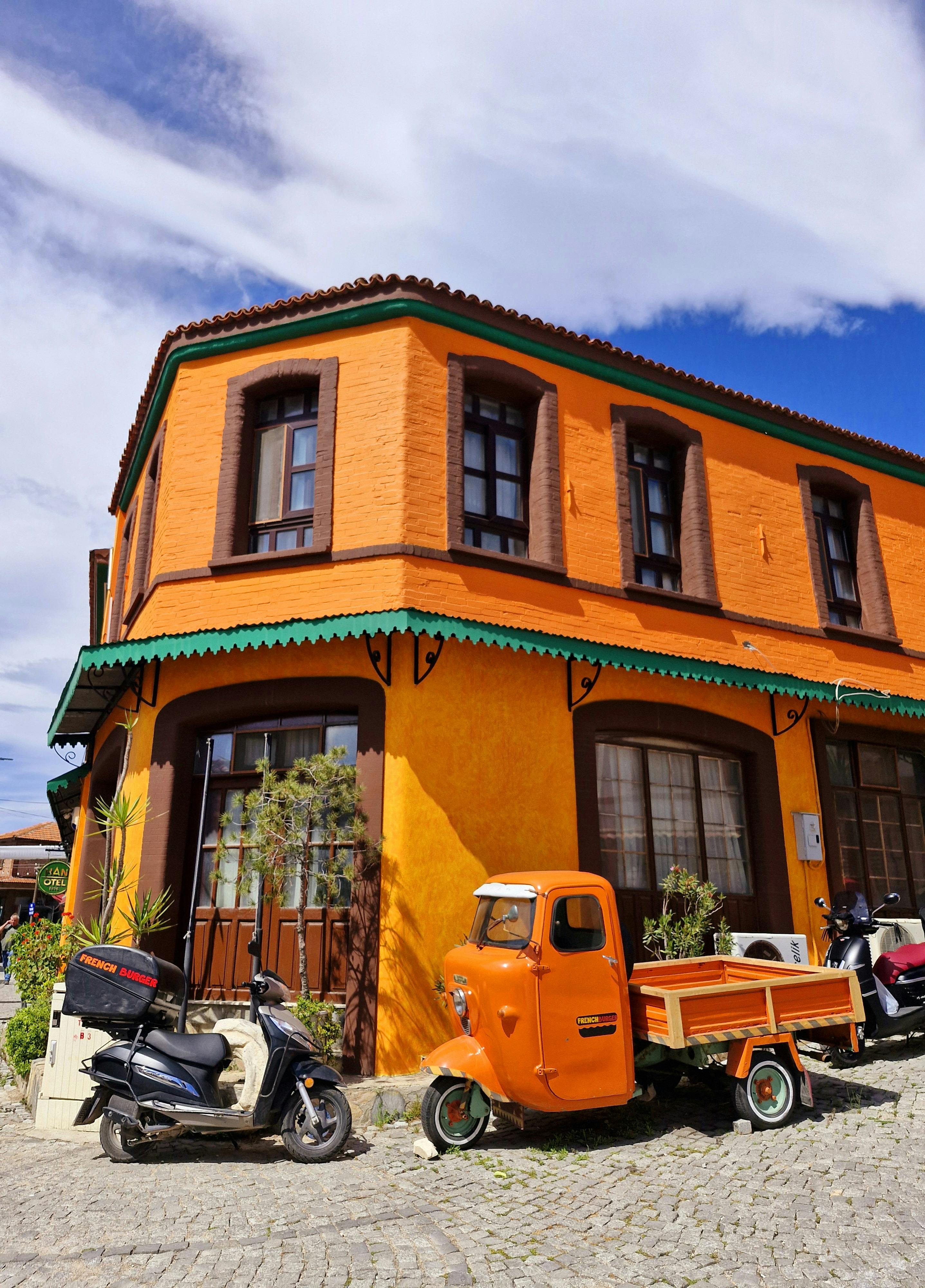 Bright orange building with scooters and a tricycle in a sunny urban setting.