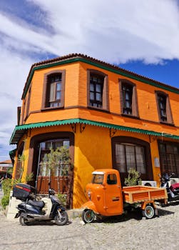 Bright orange building with scooters and a tricycle in a sunny urban setting.