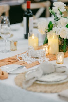 An elegant table arrangement featuring candles, flowers, pearls, and a bottle of wine.
