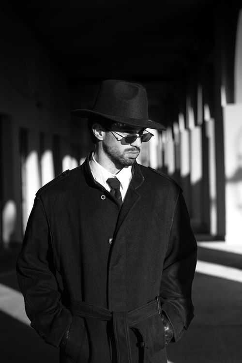 Free A stylish man in a black coat, hat, and sunglasses under dramatic light. Stock Photo