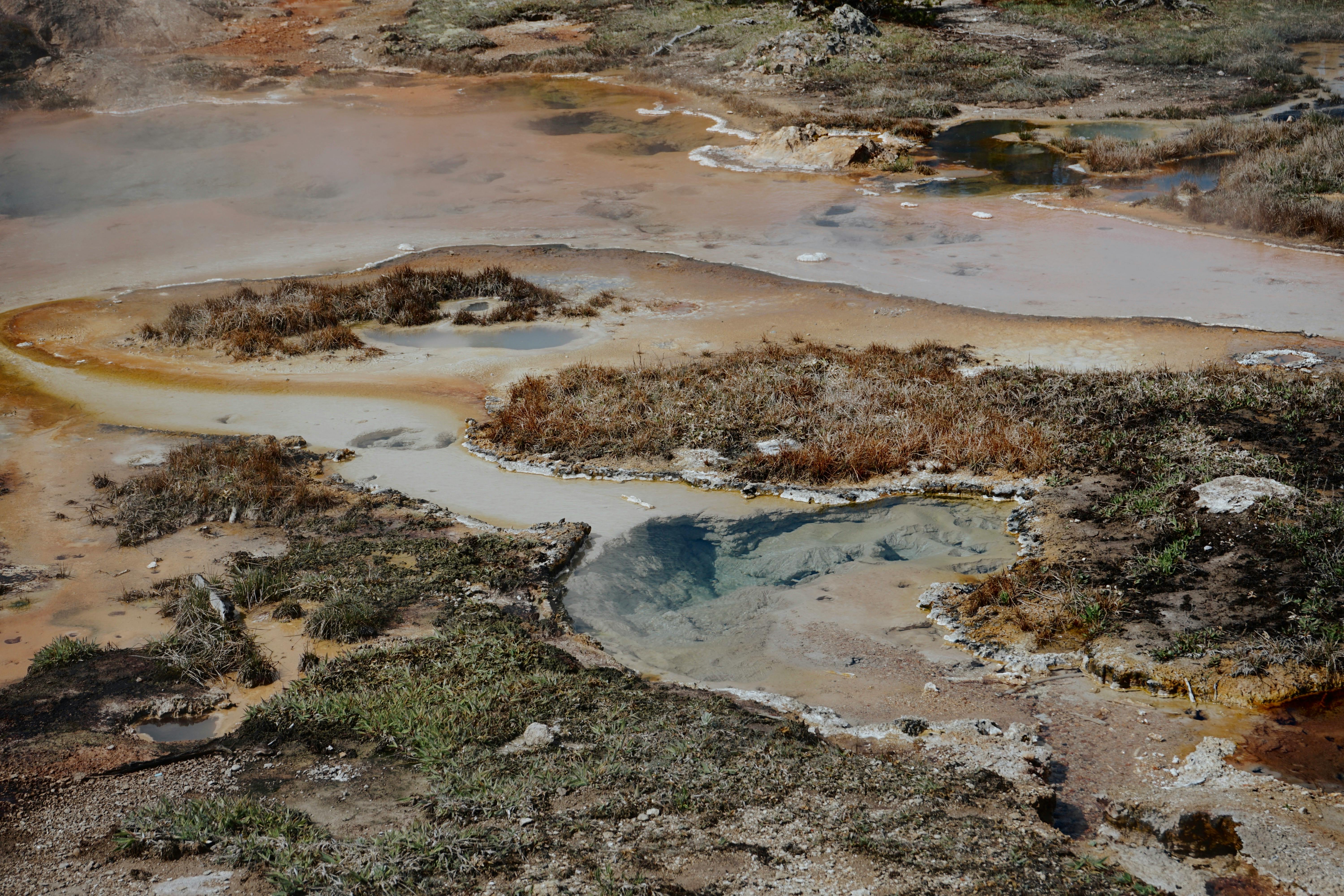 Aerial view of a geothermal hot spring featuring colorful mineral deposits and earthy tones.