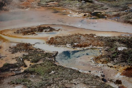 Aerial view of a geothermal hot spring featuring colorful mineral deposits and earthy tones.