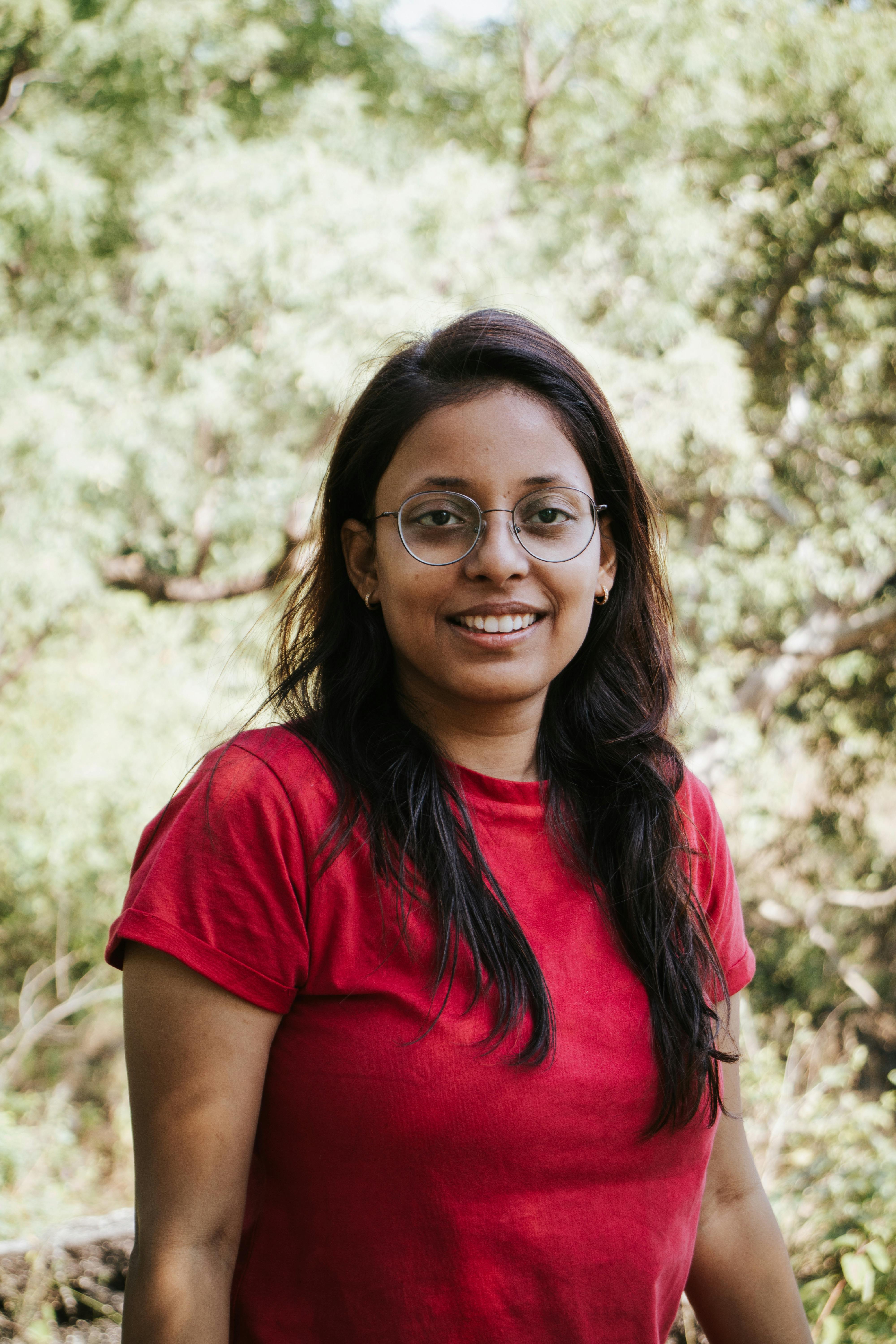 Portrait of a smiling woman in nature wearing glasses and a red shirt.