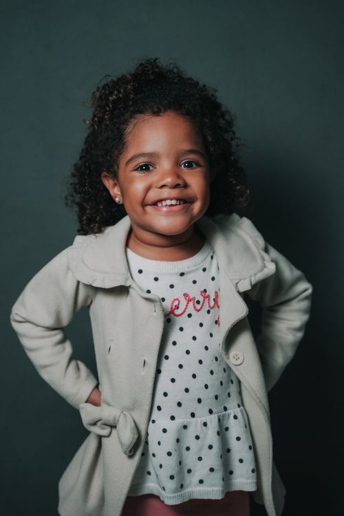 Free Cheerful young girl with curly hair and stylish outfit, smiling against a dark background. Stock Photo