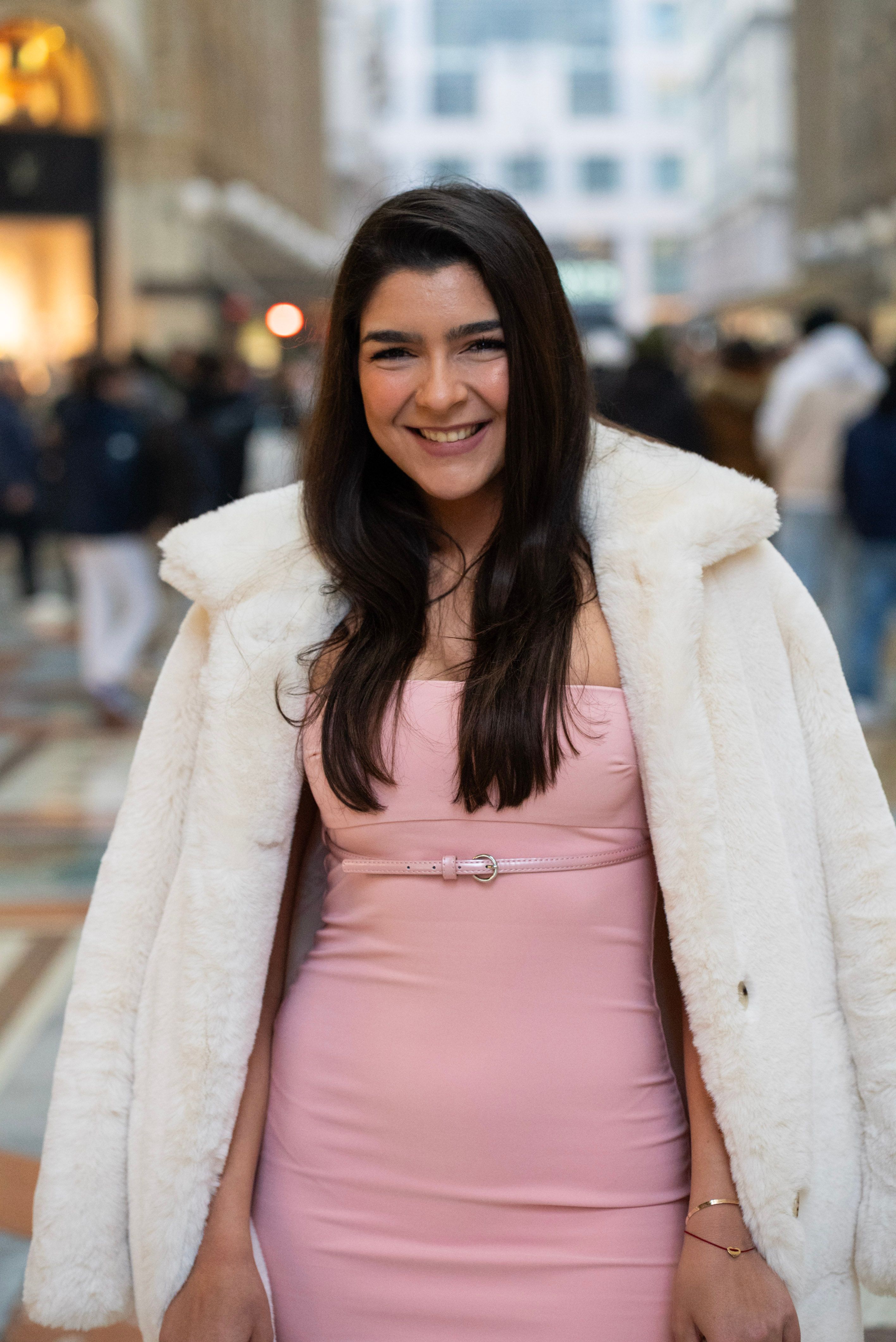 Stylish woman in a pink dress with a white coat posing at Galleria Vittorio Emanuele II in Milan.