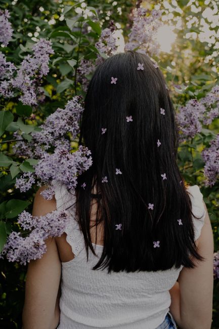 Rear view of woman with flowers in hair among blooming lilacs at sunset.