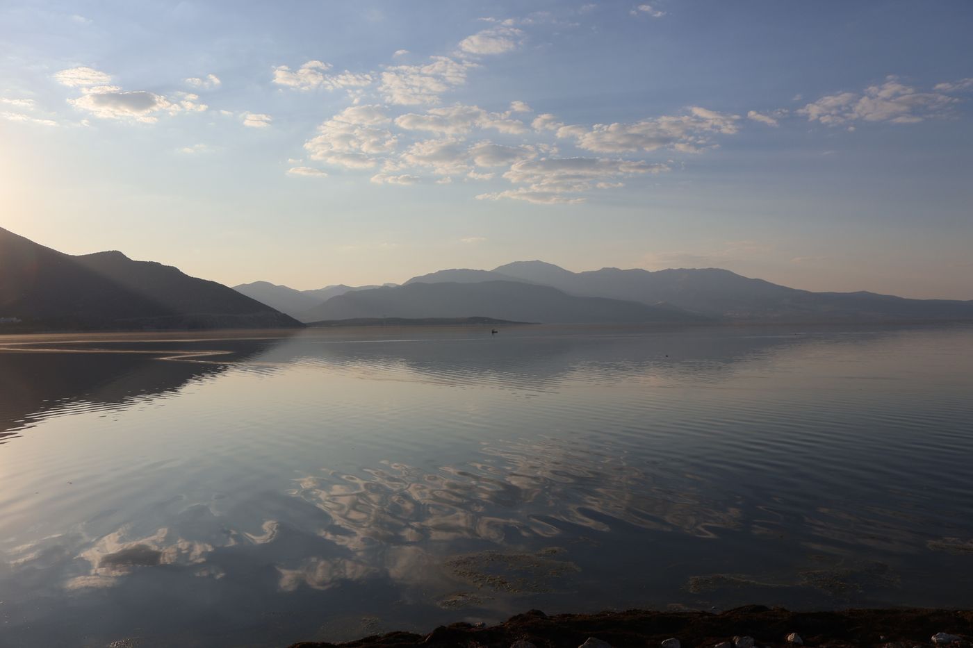 A still lake at sunrise, mountains and sky reflected in the water