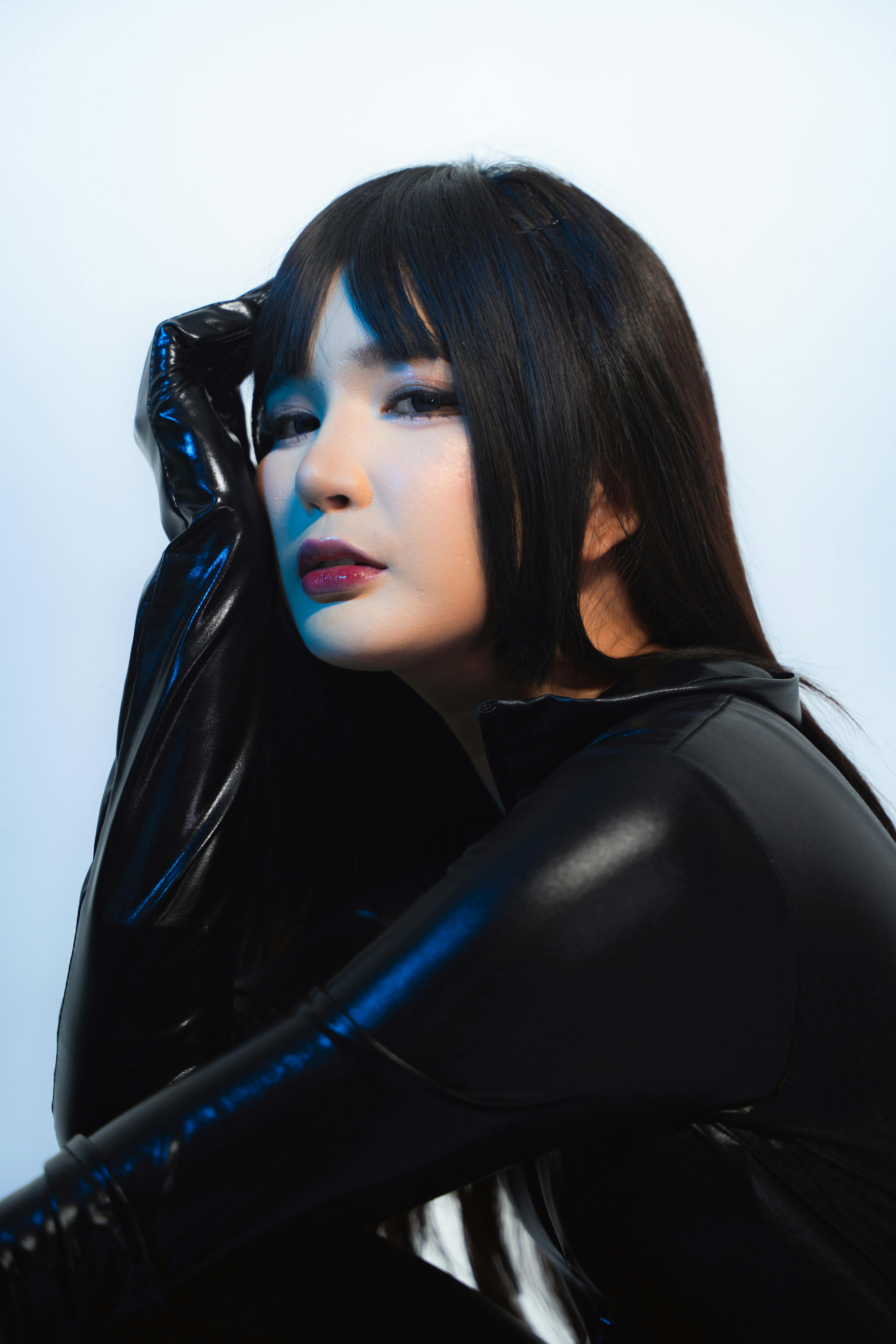 Artistic portrait of a woman wearing a black vinyl bodysuit with dramatic lighting.