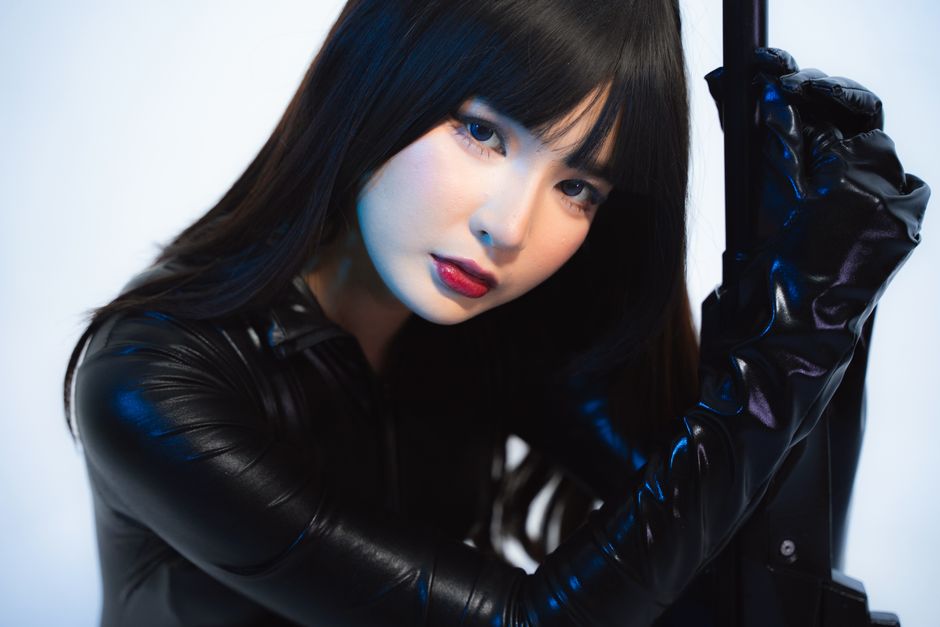 Woman in black leather outfit posing with mysterious gaze, indoors.