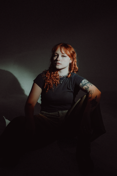 An artistic studio portrait of a redheaded woman in a moody and shadowy setting that showcases unique style and expression.