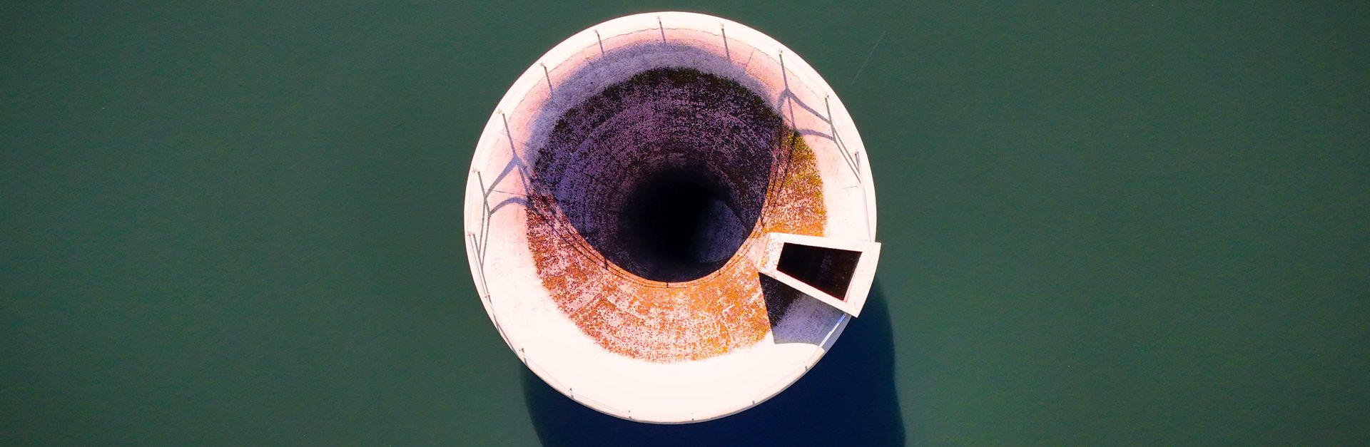 Aerial view of a bell mouth spillway in a calm reservoir, highlighting engineering and architecture.