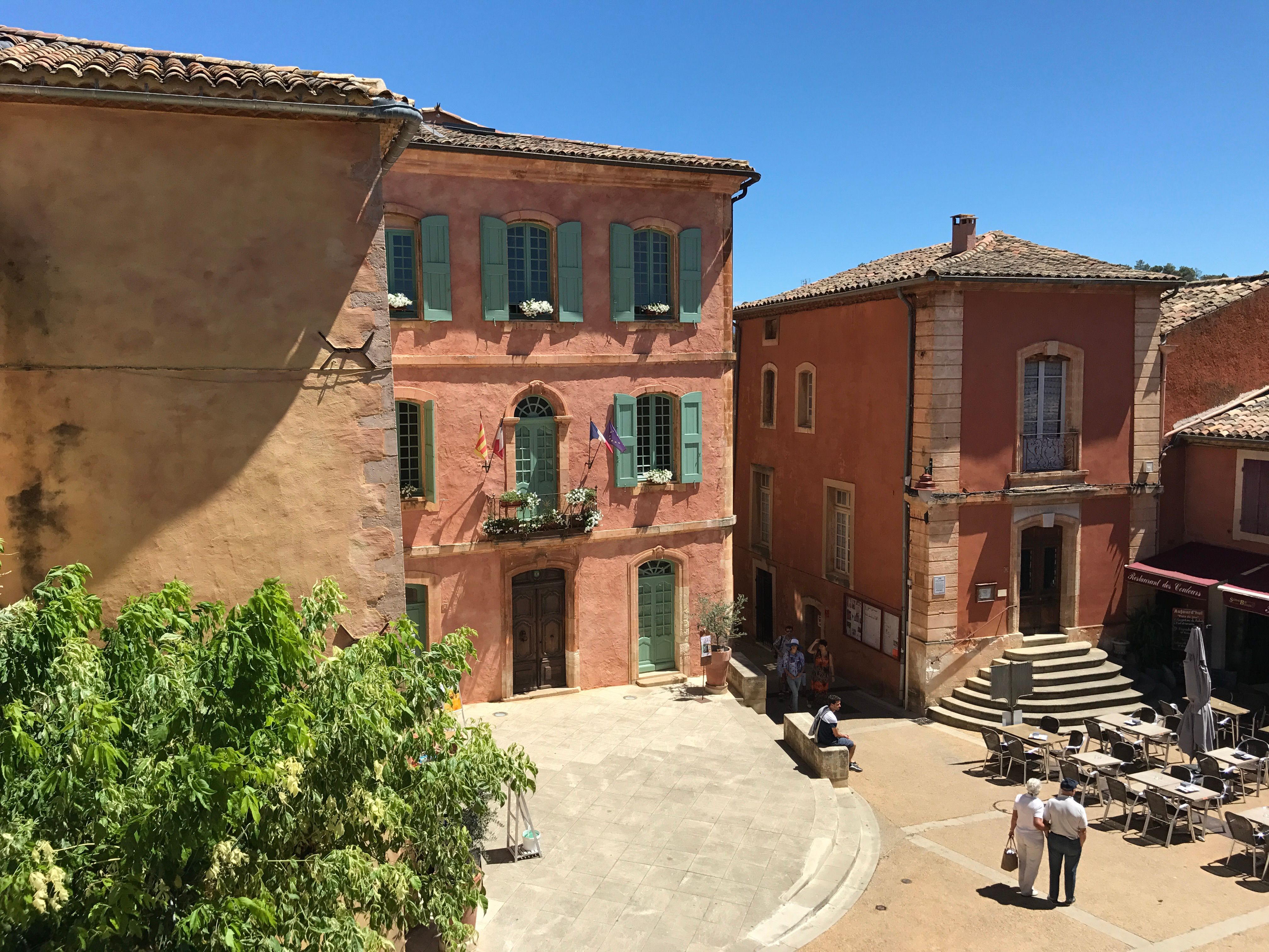 A sunny day in the vibrant town square of Roussillon, showcasing its iconic ochre buildings.