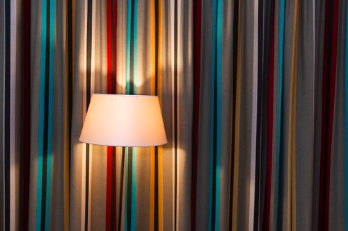 Free A white wall lamp lights up vibrant striped curtains, creating a warm ambiance. Stock Photo