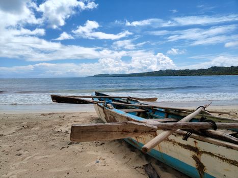 A wooden boat rests on a sandy beach against a clear blue sea and sky.