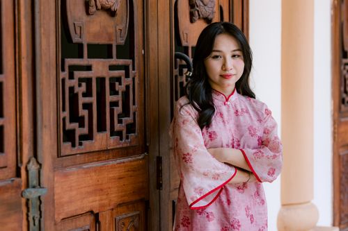 Free Elegant woman in a pink traditional Asian dress standing by ornate wooden doors indoors. Stock Photo
