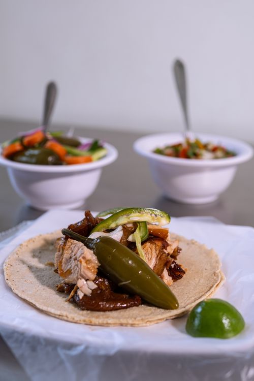 Free Close-up of a chicken taco with jalapeños, lime, and side dishes, highlighting Mexican cuisine. Stock Photo