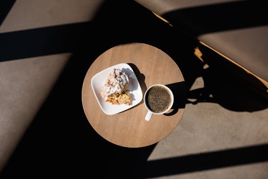 Flat lay of coffee and pastry on a round table with bright sunlight creating dramatic shadows.
