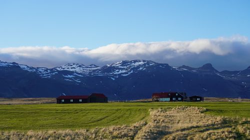 Free Idyllic scene with snow-capped mountains and houses on a vast green field under a bright blue sky. Stock Photo