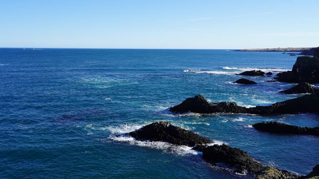 Breathtaking view of the ocean waves crashing against a rocky shoreline under a clear blue sky.